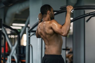 Athletic Young African American Man Pulling Up On Horizontal Bar At Gym, Black Shirtless Muscular Man Training On Modern Fitness Equipment At Sport Club, Enjoying Bodybuilding Workout, Free Space