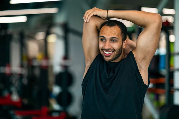 Smiling Young African American Sportsman Stretching Arm Muscles During Workout At Gym, Handsome Black Male Athlete Warming Up Before Training In Modern Fitness Club, Closeup Shot With Copy Space