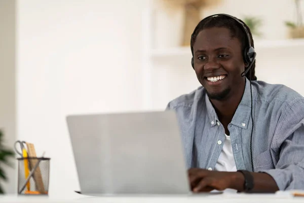 Telecommuting Concept. Smiling African American Man Wearing Headset Working With Laptop At Home Office, Happy Handsome African American Male Sitting At Desk And Looking At Computer Screen, Copy Space