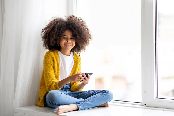 Cheerful Cute African American Little Girl Bushy Hair Sitting Windowsill — Stockfoto