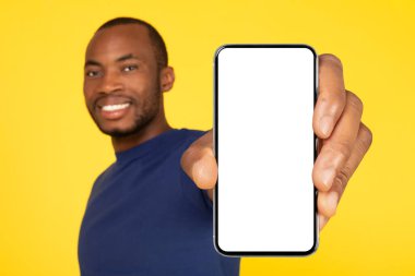 African American Guy Showing Large Cellphone With Blank Screen Recommending Application Over Yellow Studio Background. Wow Mobile Offer Advertisement. Mockup, Selective Focus