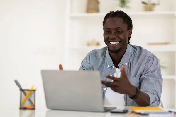 Online Meeting. Smiling Black Man Making Video Call With Laptop At Home Office, African American Male Freelancer Sitting At Desk And Talking At Computer Web Camera, Enjoying Communication, Copy Space