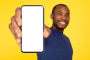 Great Application. Cheerful Black Male Showing Huge Phone With Empty Screen Smiling To Camera Over Yellow Studio Background. Mobile Offer Advertisement. Mockup