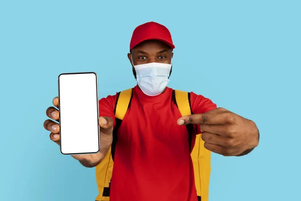 Black Young Delivery Guy Medical Mask Pointing Blank Smartphone White — Fotografia de Stock
