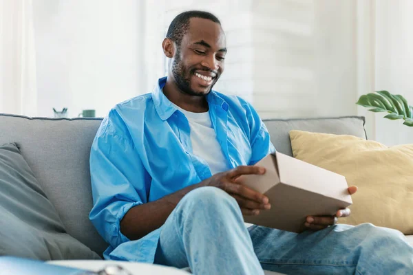 Happy Black Man Unpacking Delivery Box Sitting Sofa Smiling Male —  Fotos de Stock