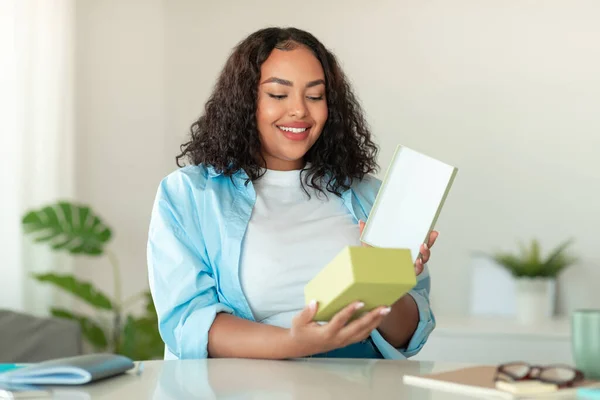Happy African American Woman Buyer Unpacking Cardboard Box Sitting At Desk At Home. Successful Shopping And Gift Delivery Service Concept. Selective Focus