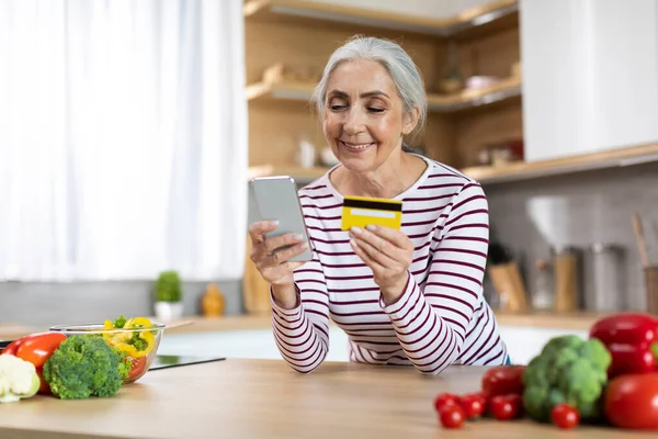 Smiling Senior Woman Using Smartphone Credit Card While Cooking Kitchen — Stockfoto