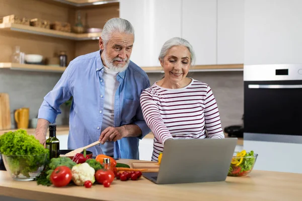 Cheerful Elderly Spouses Looking Recipe Laptop While Cooking Food Kitchen — ストック写真