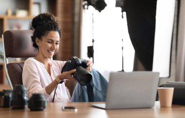 Beautiful creative young woman photographer working in office, using laptop and camera, copy space. Freelance online marketing business people employees, creative artist female business