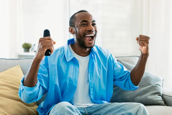 Overjoyed Black Man Watching Sport Home Celebrating Success Raising Fists — Stok fotoğraf