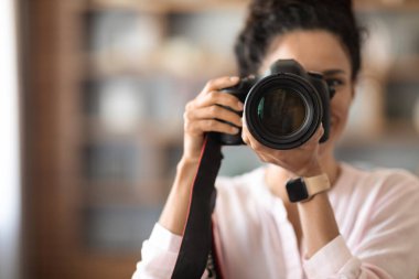 Pretty brunette woman professional photographer holding dslr camera, office or home interior, blurred background, closeup photo, copy space. Jobs and occupations concept