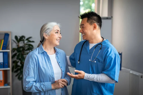 Cheerful Millennial Japanese Man Doctor Meets Talks Aged Female Patient — Zdjęcie stockowe