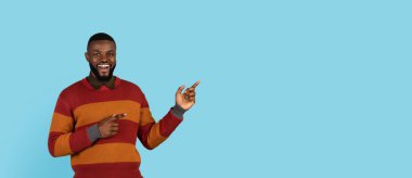 Look There. Smiling black man pointing aside at copy space on blue background with two hands, handsome young african american male demonstrating free place for your advertisement or design, panorama