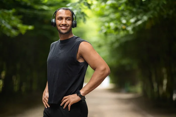 Cheerful Young Black Guy Athlete Listening Music While Jogging Public — Stok fotoğraf