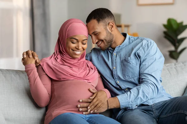 Happy Married Black Muslim Couple Expecting Baby Cuddling Couch Living — Stock fotografie