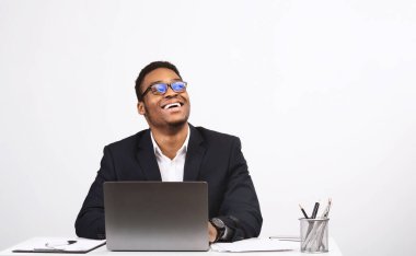 Excited African American Businessman Using Laptop Computer Working Online Sitting At Desk Over White Studio Background. Internet Technology And Business Concept