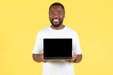 Happy Black Guy Showing Laptop Computer With Blank Screen Advertising Great Website Smiling To Camera Standing Over Yellow Studio Background. Internet Technology. Mockup