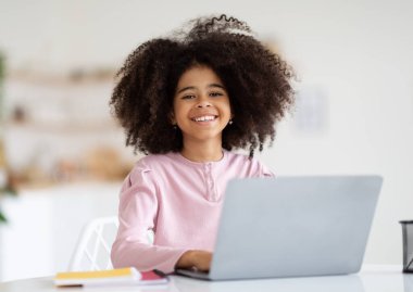 Cute cheerful african american little school girl typing on laptop keyboard, schooler doing homework, preteen kid working on educational project, copy space. Home schooling, e-education concept