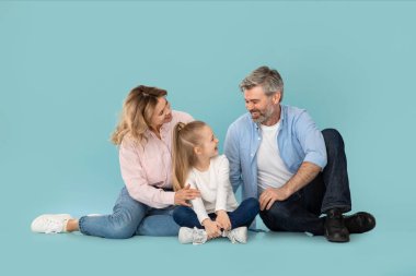 Family Communication. Happy Middle Aged Parents Talking To Little Daughter Laughing Together Sitting Over Blue Background. Joy Of Parenthood. Studio Shot, Full Length