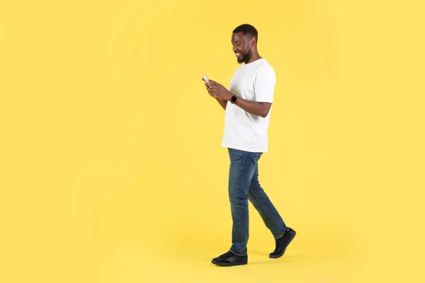 African American Guy Using Cellphone Texting Walking Posing Studio Yellow — Stockfoto