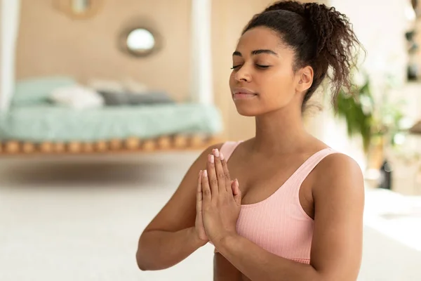 Mind harmony. Portrait of calm black lady meditating with closed eyes, practicing meditation or praying, keeping hands in namaste gesture, free space