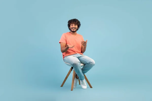 Cheerful Eastern Guy Casual Outfit Sitting Chair Blue Studio Background — Stok fotoğraf