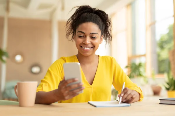 Remote Learning Happy Black Woman Using Smartphone Writing Her Notebook — Fotografia de Stock