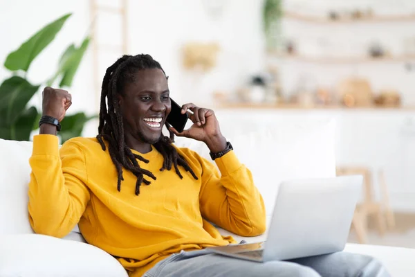 Overjoyed Black Guy Sitting Laptop Couch Talking Cellphone Excited Young —  Fotos de Stock