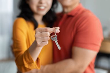 Unrecognizable asian couple standing and hugging together and holding house key, enjoying moving to their new house to start new life. Family, age, home, real estate and people concept