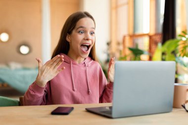 Wow. Surprised teenage girl using laptop looking at screen with open mouth in amazement, reading news or getting A-grade, sitting at table at home