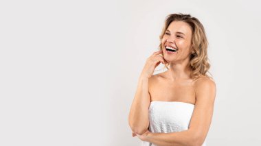 Body Care. Portrait Of Joyful Beautiful Middle Aged Woman Wrapped In Bath Towel, Happy Attractive Mature Lady Laughing While Posing Over Light Grey Studio Background, Panorama With Copy Space
