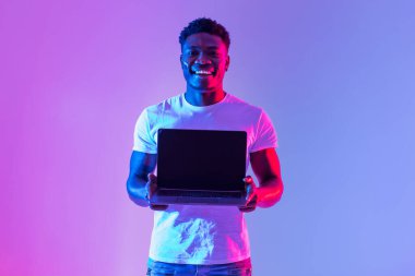Check this website. Handsome young black man holding laptop with blank screen in neon light, mockup for design. Happy African American male showing empty space for online ad