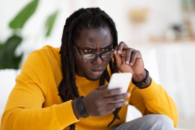Eyesight Problems Concept. Young Black Man Wearing Eyeglasses Reading Message On Smartphone, African American Guy Looking At Cellphone Screen, Taking Off Glasses And Squinting Eyes, Closeup