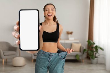 Weight Loss App. Happy Slim African American Woman Wearing Large Jeans Showing Blank Smartphone With White Screen, Smiling Black Female Recommending Dieting Application, Mockup, Collage