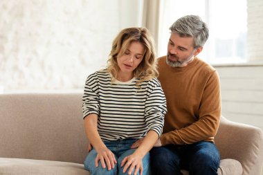 Husband Hugging Sick Wife While She Feels Bad Supporting And Helping Her Sitting On Sofa At Home. Female Health Problems, Healthcare And Illness Symptoms Concept