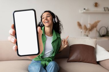 Music App. Cheerful Young Woman In Wireless Headphones Holding Big Blank Smartphone In Hand, Singing And Having Fun At Home, Happy Carefree Female Listening Favorite Playlist, Collage, Mockup