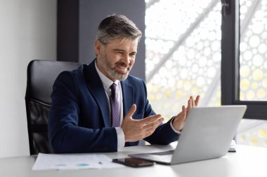 Video Conference. Handsome Middle Aged Businessman Having Web Call With Client, Smiling Male Entrepreneur In Suit Using Laptop For Online Communication, Talking And Gesturing At Camera, Free Space