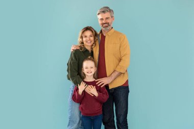 Family Concept. Cheerful Middle Aged Parents And Little Kid Daughter Hugging Over Blue Background In Studio. Daddy And Mommy Posing With Their Child Smiling To Camera