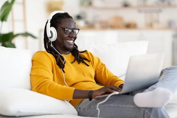 Smiling Young Black Man Wearing Wireless Headphones Relaxing Laptop Home — Fotografia de Stock