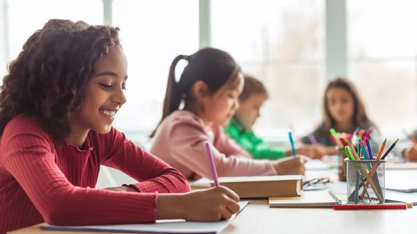 Black Schoolgirl Writing Sitting Desk Learning Multicultural Classmates Having Class — Stockfoto