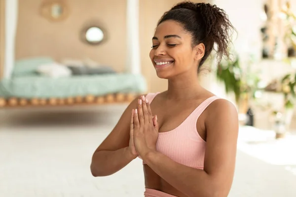 Concentration concept. Happy african american lady with closed eyes holding hands in prayer pose, meditating for mental health and smiling, copy space