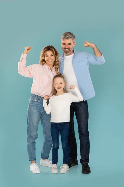 We Are Strong. Happy Family Of Three Showing Biceps Muscles Posing Together Smiling To Camera Standing Over Blue Studio Background. Strength And Power Concept. Vertical Shot