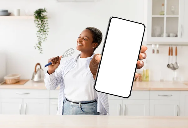 Food Delivery App. Cheerful Black Lady Standing In Kitchen With Big Blank Smartphone In Hand, Happy Young African American Woman Demonstrating New Mobile Application Or Website, Collage, Mockup