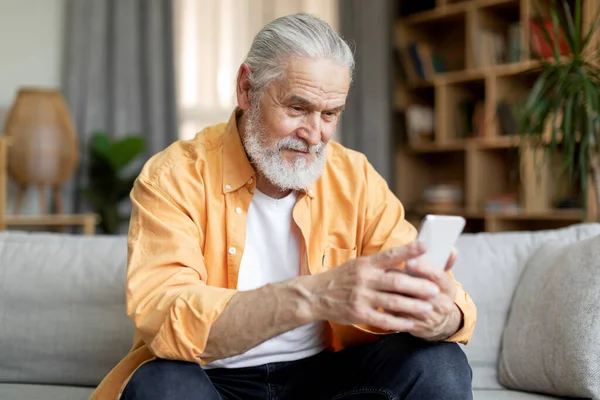 Happy Handsome Senior Man Sitting Couch Home Using Modern Smartphone — Stok fotoğraf
