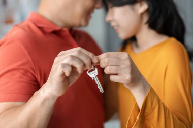 Cropped of chinese husband and wife holding together key from their new house and cuddling, asian family moving to new apartment. Mortgage, real estate, moving, relocation concept