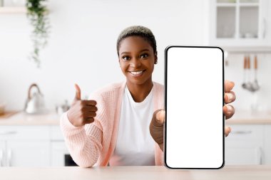 Smiling Black Woman Holding Big Blank Smartphone In Kitchen And Showing Thumb Up Gesture, Happy Young African American Female Recommending New Mobile Application Or Website, Collage, Mockup
