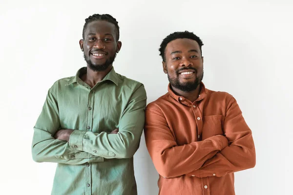 Two Smiling Black Men Posing Standing Crossing Hands Looking At Camera Over White Background. Studio Shot Of Male Friends Expressing Positive Emotions. Confidence And Friendship Concept
