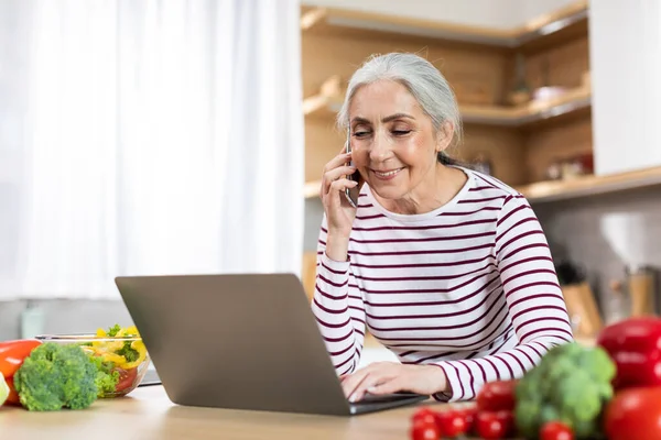 Beautiful Senior Woman Talking Cellphone Using Laptop Kitchen Smiling Elderly — Stockfoto