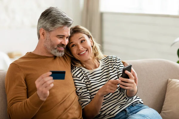 Happy Spouses Shopping Online Phone Holding Credit Card Sitting Sofa — Φωτογραφία Αρχείου