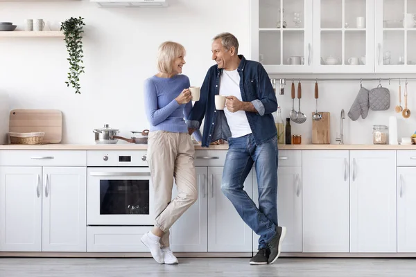 Happy Attractive Senior Couple Homewear Standing White Cozy Kitchen Drinking — Foto de Stock